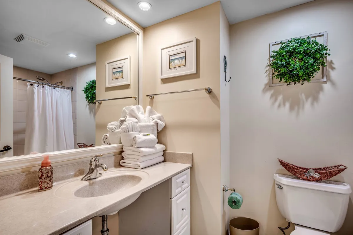 A bright, serene laundry space featuring a vanity with sink, fluffy towels, framed artwork, and decorative greenery. This space feels both functional and inviting, supporting longer and more comfortable stays.